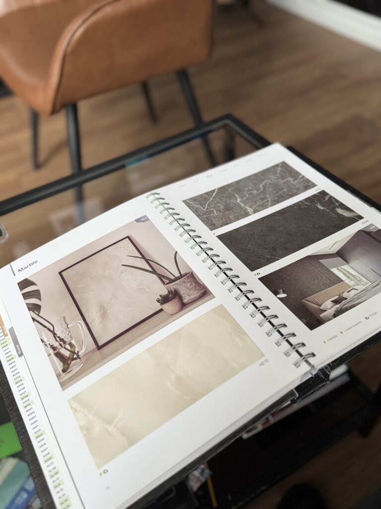 Open material sample book displaying marble vinyl wrap textures on a table at WrapStyle Home in Ontario.